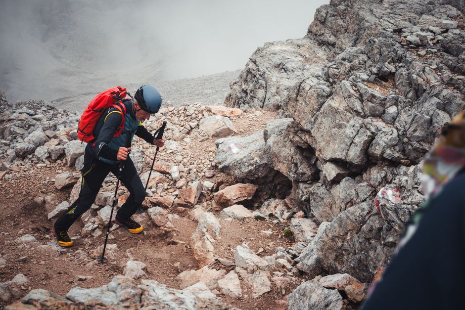 A determined hiker conquering a rocky mountain trail with trekking poles and helmet, showcasing adventure.