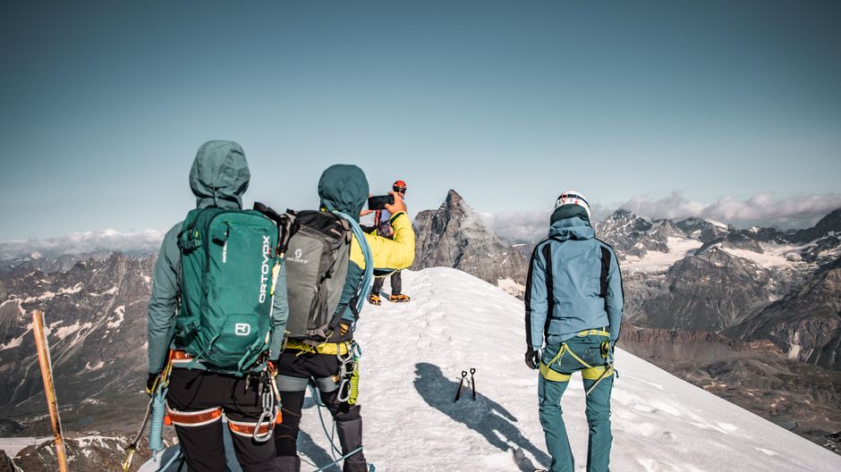 Climbers reaching the snowy summit of a mountain in Zermatt, Switzerland with breathtaking views.